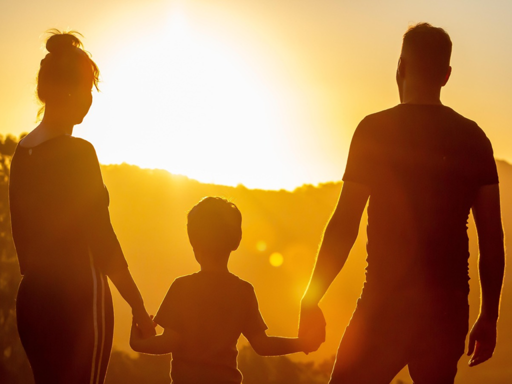 deux parents qui tienne les mains de leur fils en regardant le coucher de soleil